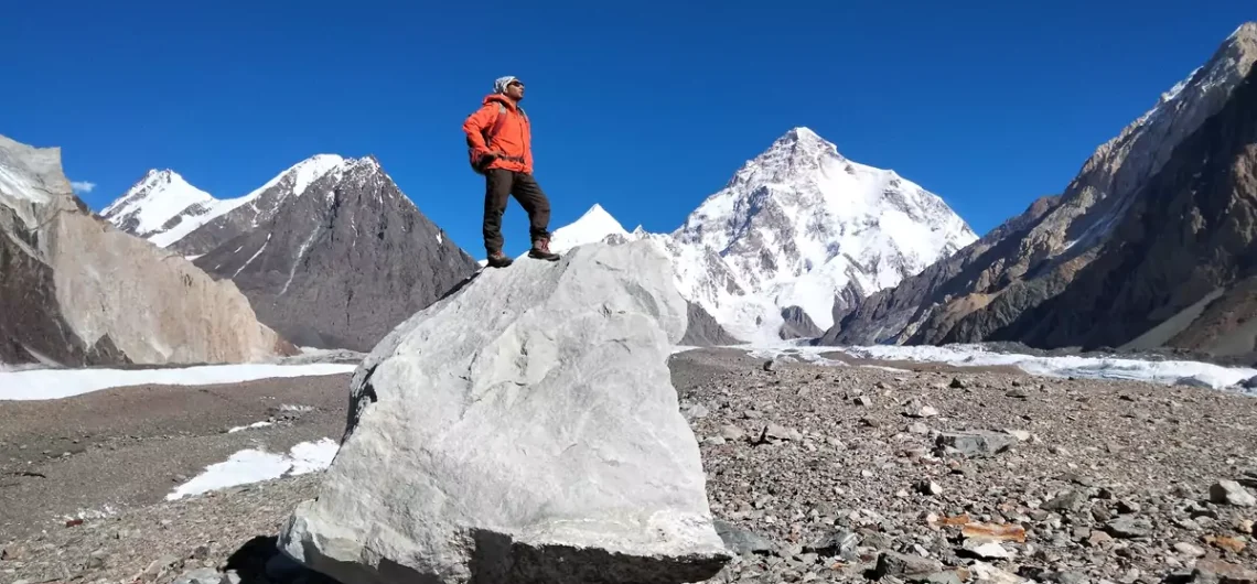 A trekker sitting on a rock with a stunning view of K2 in the background during the K2 Base Camp trek